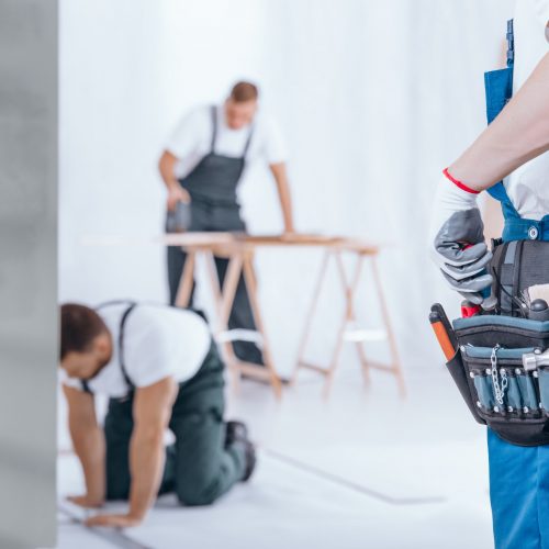 Close-up of handyman with glove on hand and tool belt on blue trousers during home renovation