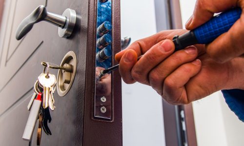 Repairman is standing in the hallway and fixing the door lock with screwdriver